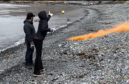 Bo Whiteside left and a Region IV fishery biologist deploy a smoke cannister on a beach in Dutch Harbor April 2023 part of the signaling module of marine safety training