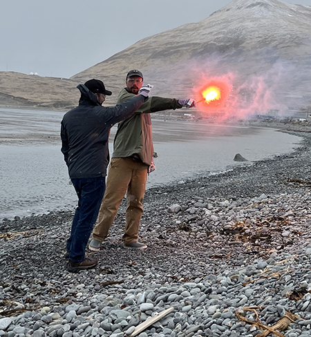 A fishery biologist learns to safely use a handheld flare on a beach in Dutch Harbor April 2023